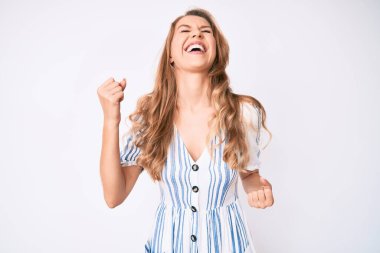 Sarı saçlı, yaz elbisesi giyen genç beyaz kadın kolları havada ve gözleri kapalı bir şekilde başarıyı kutluyor ve şaşırıyor. 