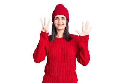 Süveter ve yün şapka giyen genç ve güzel bir kız sekiz numaralı parmaklarıyla gülümseyerek, kendinden emin ve mutlu görünüyor.. 