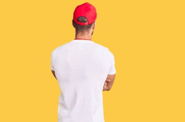 Can kurtaran tişörtü giyen genç beyaz bir adam ıslık çalıp arkaya bakıyor ve kollarını kavuşturuyor. 