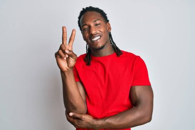 Saçları günlük kıyafetlerle örülmüş, kameraya gülümseyen ve zafer işareti yapan Afro-Amerikan bir adam. İki numara.. 