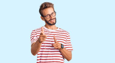 Sıradan kıyafetler ve gözlük takan sakallı yakışıklı sarışın adam mutlu ve komik yüzüyle kamerayı işaret ediyor. iyi enerji ve titreşimler. 