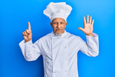 Orta yaşlı, gri saçlı, profesyonel aşçı üniforması giyen ve şapkasını altı numaralı parmaklarıyla gösteren mutlu ve kendinden emin bir şekilde gülümseyen adam.. 