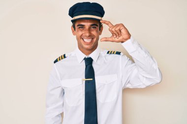 İspanyol asıllı genç adam, uçak pilotu üniforması giyiyor gülümsüyor ve el hareketleriyle el hareketi yapıyor parmaklarıyla işaret yapıyor ve kameraya bakıyor. ölçüm kavramı. 