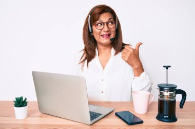 Orta yaşlı esmer, ofiste çalışan, operatör kulaklığı takan, ağzı açık gülümseyen bir kadın. 