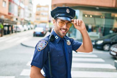 Polis üniforması giyen genç, yakışıklı İspanyol polis mutlu bir şekilde gülümsüyor..