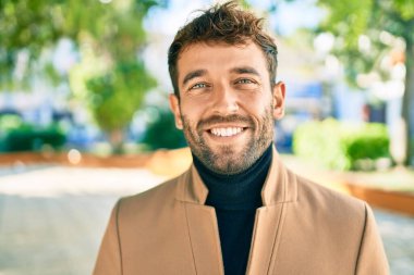 Zarif ceket giyen yakışıklı iş adamı dışarıda mutlu bir şekilde gülümsüyor.