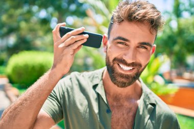 Genç İspanyol adam parkta yürürken mutlu bir şekilde gülümsüyor.