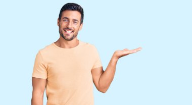 Gündelik kıyafetler giyen genç İspanyol adam neşeli bir şekilde gülümsüyor ve avuç içi kameraya bakıyor.. 