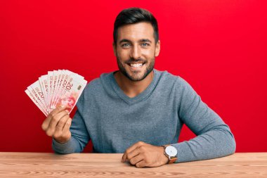 Yakışıklı İspanyol adam İsrail şekellerini tutuyor. Pozitif ve mutlu görünüyor. Kendine güvenen bir gülümsemeyle dişlerini gösteriyor. 