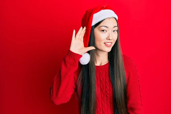 若い中国の女性は 耳を傾け 噂やゴシップに耳を傾け手で笑みを浮かべてクリスマスの帽子をかぶって 聴覚障害の概念 — ストック写真