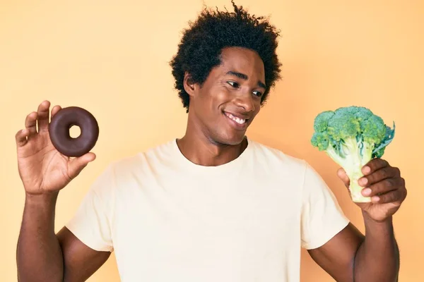 Pohledný Africký Američan Afro Vlasy Drží Brokolici Čokoládové Koblihy Úsměvem — Stock fotografie