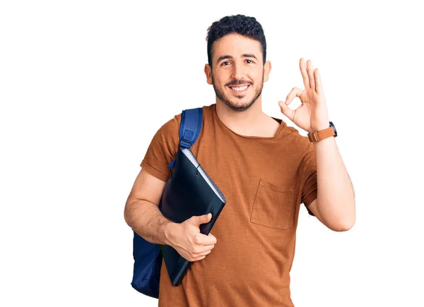若いヒスパニック系の男は 指でOkサインを行うバインダーを保持学生のバックパックを身に着けています 笑顔優しいジェスチャー優れたシンボル — ストック写真
