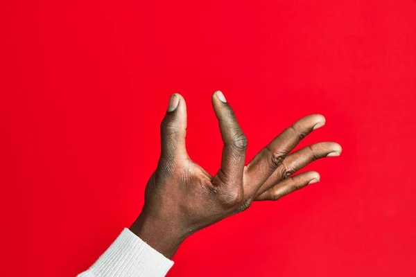 Arm and hand of african american black young man over red isolated background picking and taking invisible thing, holding object with fingers showing space