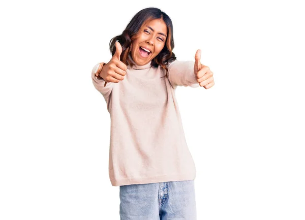 年轻美丽的混血女子身穿冬季高领毛衣 手握积极的手势 微笑着竖起大拇指 为成功感到高兴 优胜手势 — 图库照片