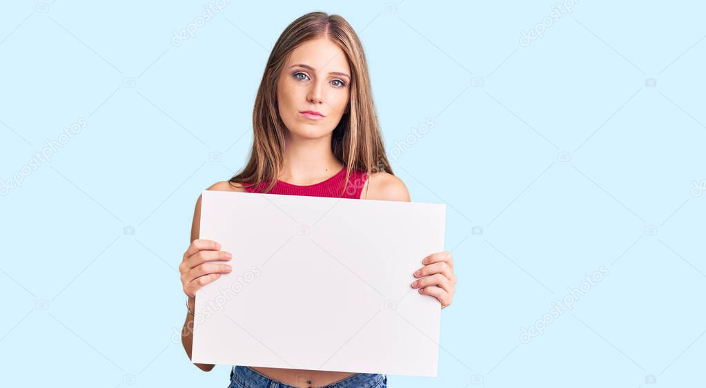 Young beautiful blonde woman holding blank empty banner thinking attitude and sober expression looking self confident 
