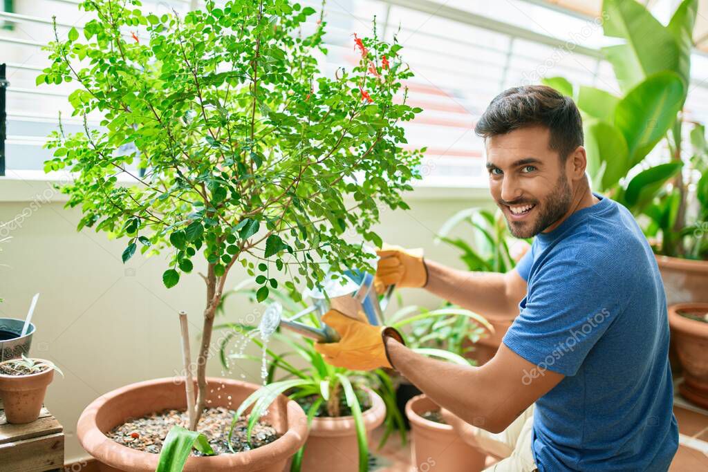 Young handsome man smiling happy caring plants using watering can at terrace
