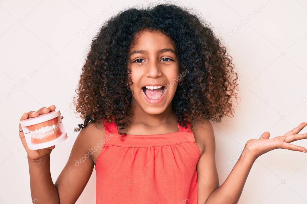 African american child with curly hair holding denture celebrating victory with happy smile and winner expression with raised hands 