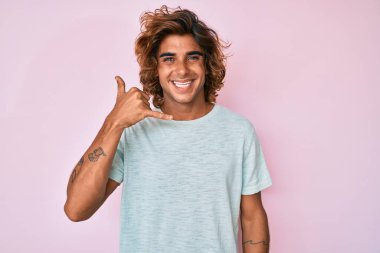 Günlük kıyafetler giymiş, gülümseyen genç İspanyol adam telefonla el ve parmak hareketleri yapıyor telefonda konuşur gibi. iletişim kavramları. 