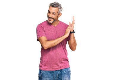 Orta yaşlı, gri saçlı, sıradan kıyafetler giyen, alkışlayan mutlu ve neşeli, gururlu elleri bir arada tutan bir adam. 