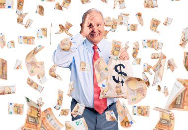 Üst düzey yakışıklı, gri saçlı, şık kıyafetler giyen, para çantası tutan mutlu mesut gülümseyen, el pençe divan duran bir adam.