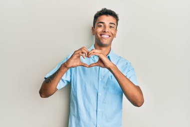 Genç, yakışıklı, Afro-Amerikan bir adam. Günlük kıyafetler giyip, aşkla gülümsüyor. Elleriyle kalp sembolü ve şekli gösteriyor. romantik kavram. 