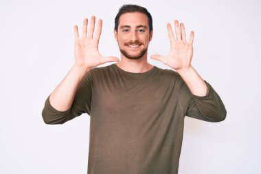 Genç ve yakışıklı bir adam günlük kıyafetler giyer ve 10 numarayı göstererek gülümserken kendinden emin ve mutluydu.. 