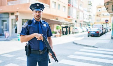Polis üniforması giyen genç, yakışıklı İspanyol bir polis memuru. Elinde ciddi bir ifade var..