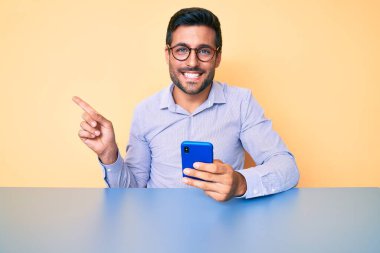 Genç İspanyol adam akıllı telefon kullanıyor masaya oturmuş gülümsüyor mutlu bir şekilde elini ve parmağını yana uzatıyordu. 