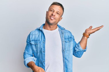 Yakışıklı, sıradan bir kot ceket giyen, neşeli bir şekilde gülümseyen, avuç içiyle kameraya bakan kaslı adam.. 