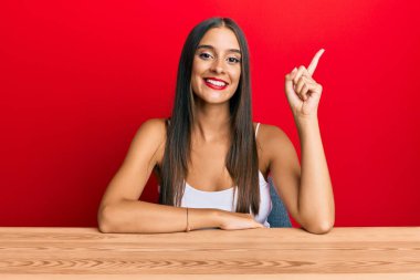 Genç İspanyol kadın gündelik giysiler içinde masaya oturmuş gülümsüyor mutlu bir şekilde elini ve parmağını yana doğru uzatıyordu. 