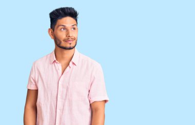 Yakışıklı Latin Amerikalı genç adam, sıradan bir yaz gömleği giyiyor. Gülümsüyor, yan tarafa bakıyor ve düşünüyor.. 