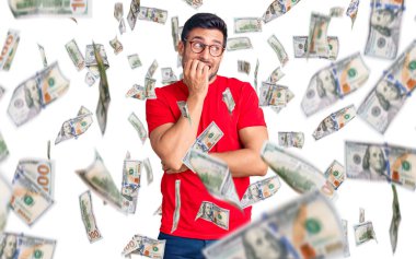 Günlük kıyafetler ve gözlük takan genç İspanyol adam gergin ve gergin görünüyor. Elleri ağızda, tırnaklarını yiyor. anksiyete.