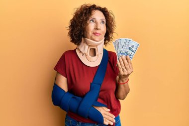 Güzel, orta yaşlı, olgun bir kadın. Servikal tasma takıyor ve elinde sigorta dolarları tutuyor. Gülümsüyor ve başka tarafa bakıyor.. 