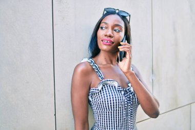 Genç Afrikalı Amerikalı kadın akıllı telefondan konuşuyor. Şehrin caddesinde duvara yaslanıyor.