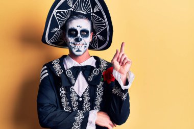 Meksika 'daki ölü kostümünü giyen genç adam sarıya gülümseyen mutlu bir şekilde elini ve parmağını yana doğru uzattı. 