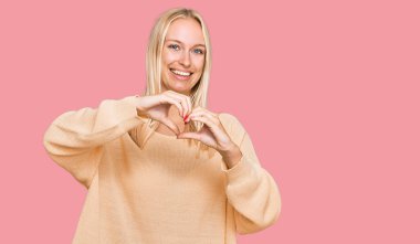 Sıradan kıyafetler giyen, aşık gülümseyen, elleriyle kalp sembolü yapan genç sarışın kız. romantik kavram. 