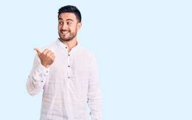 Genç, yakışıklı, sıradan kıyafetler giyen, gülen yüzlü, gülümseyen ve baş parmağıyla yan tarafı gösteren bir adam.. 