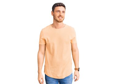 Ayılı yakışıklı, sarı tişörtlü, yüzünde gülümseme ve doğal ifadeyle yan yana bakan genç bir adam. Kendinden emin gülen. 