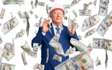 Kıdemli yakışıklı, gri saçlı, takım elbiseli, mimar şapkalı rahat ve gözleri kapalı gülümseyen parmaklarıyla meditasyon hareketi yapan adam. yoga konsepti.