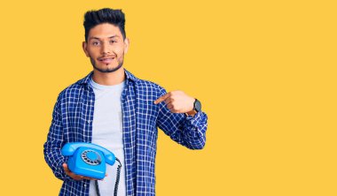 Yakışıklı Latin Amerikalı genç adam elinde antika bir telefonla gülümseyen mutlu ve gururlu birini işaret ediyor. 