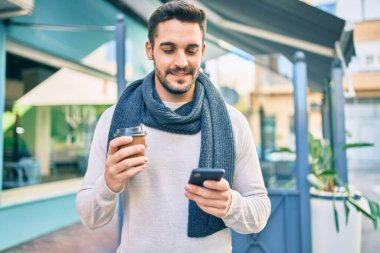 Genç İspanyol adam mutlu bir şekilde gülümsüyor. Akıllı telefon kullanıyor ve şehirde kahve içiyor..