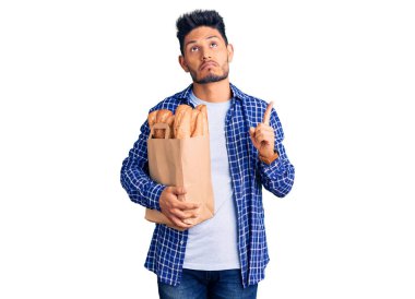 Elinde ekmek torbası olan yakışıklı Latin Amerikalı genç adam üzgün ve üzgün görünüyor, parmaklarıyla yönü gösteriyor, mutsuz ve depresif.. 