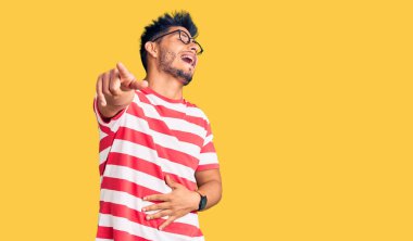 Yakışıklı Latin Amerikalı gündelik kıyafet ve gözlük takan genç adam sana gülüyor, kamerayı işaret ediyor, vücudunu gösteriyor, utanç ifadesi. 