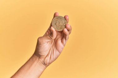 Genç İspanyol el, bitcoin 'i izole edilmiş sarı arka planda tutuyor..