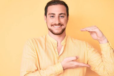 Elleriyle el kol hareketi yapan, büyük ve büyük beden işareti gösteren sıradan kıyafetler giyen genç yakışıklı bir adam. Kameraya bakıp gülümsüyor. ölçüm kavramı. 