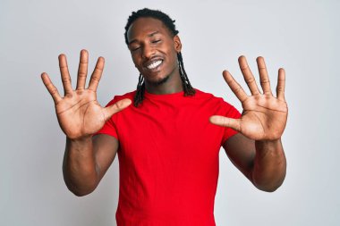 Saçları örgülü Afro-Amerikan bir adam 10 numarayı gösterip gösterirken kendinden emin ve mutlu bir şekilde gülümsüyor.. 