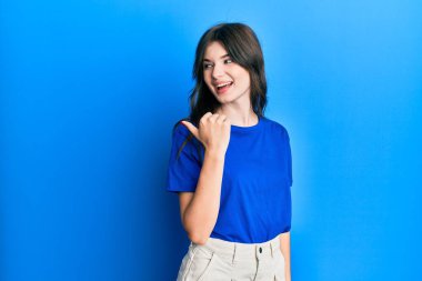 Gündelik giysiler içinde genç, güzel beyaz bir kız başparmağını yana kaldırmış, ağzı açık gülümsüyor. 