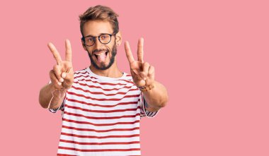 Sakallı, sıradan kıyafetler ve gözlük takan, ağzı açık gülümseyen, iki elini de zafer işareti yapan yakışıklı sarışın adam. İki numara.. 