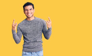 İspanyol yakışıklı genç adam gündelik kazak giyip çılgın bir ifadeyle bağırıyor elleri havada rock sembolü yapıyor. Müzik yıldızı. ağır kavram. 