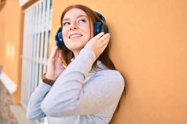 Genç İrlandalı kız gülümseyerek şehirde kulaklık takarak müzik dinliyor..